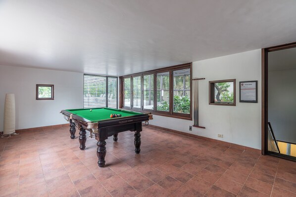 A spacious room with a pool table, large windows, and a view of greenery outside.