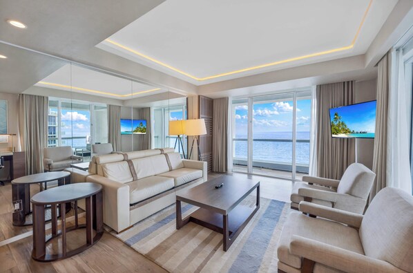 Een moderne hotelkamer met een groot raam met uitzicht op zee, een bank, een salontafel en een televisie.