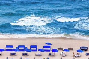 Een strand met rijen blauwe parasols en ligbedden gericht op de zee.