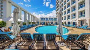 A rooftop pool area with blue lounge chairs and umbrellas, surrounded by a modern building with balconies. - Holiday Waves: Oceanview Charm at Central Beach (Fort Lauderdale)