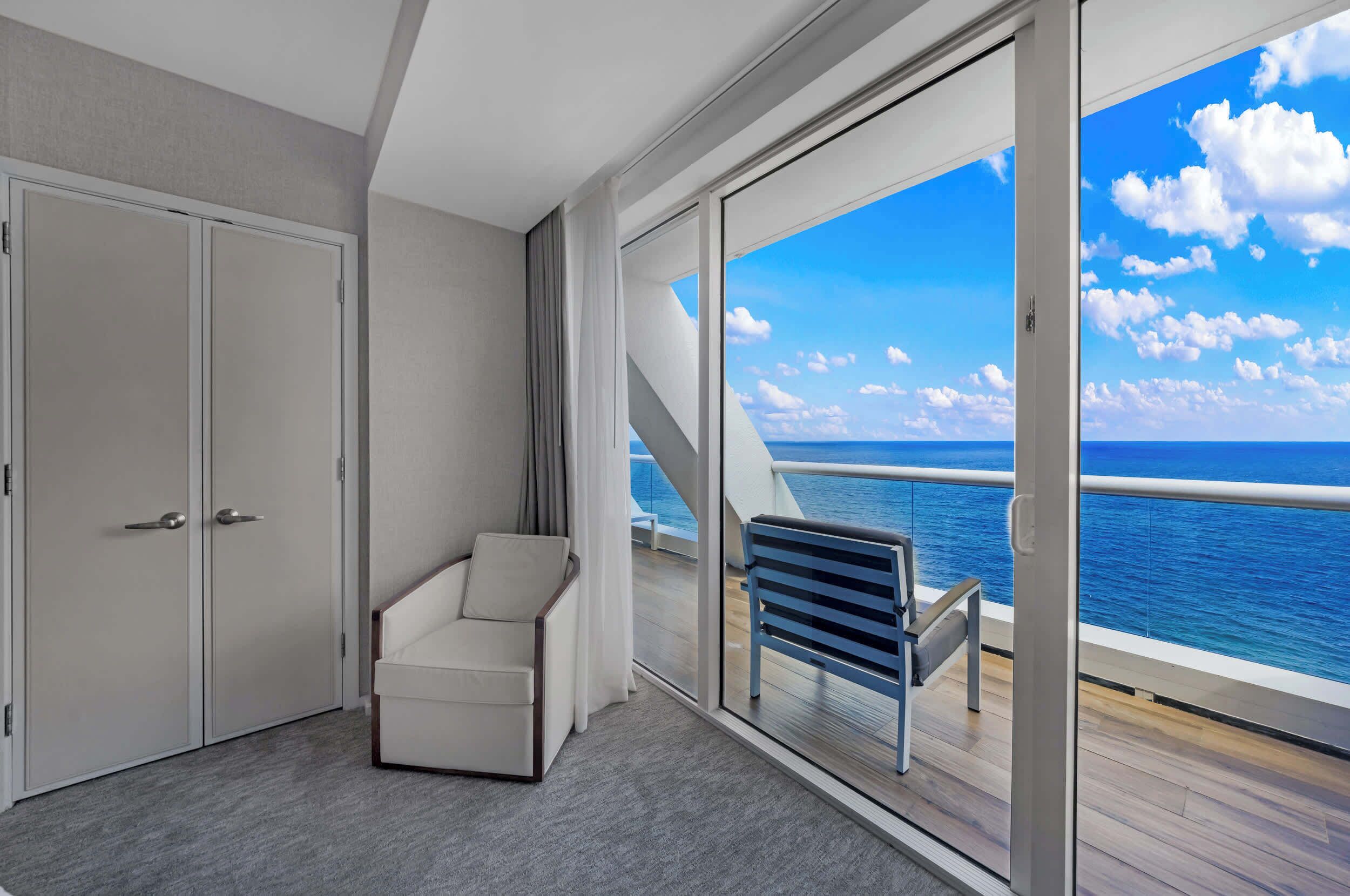 Et værelse med en stor skydedør, der fører ud til en balkon med havudsigt.