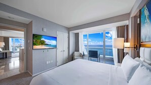 A hotel room with a large bed, a TV displaying a beach scene, a balcony with a view of the sea, and a desk with a chair. - Holiday Waves: Oceanview Charm at Central Beach (Fort Lauderdale)