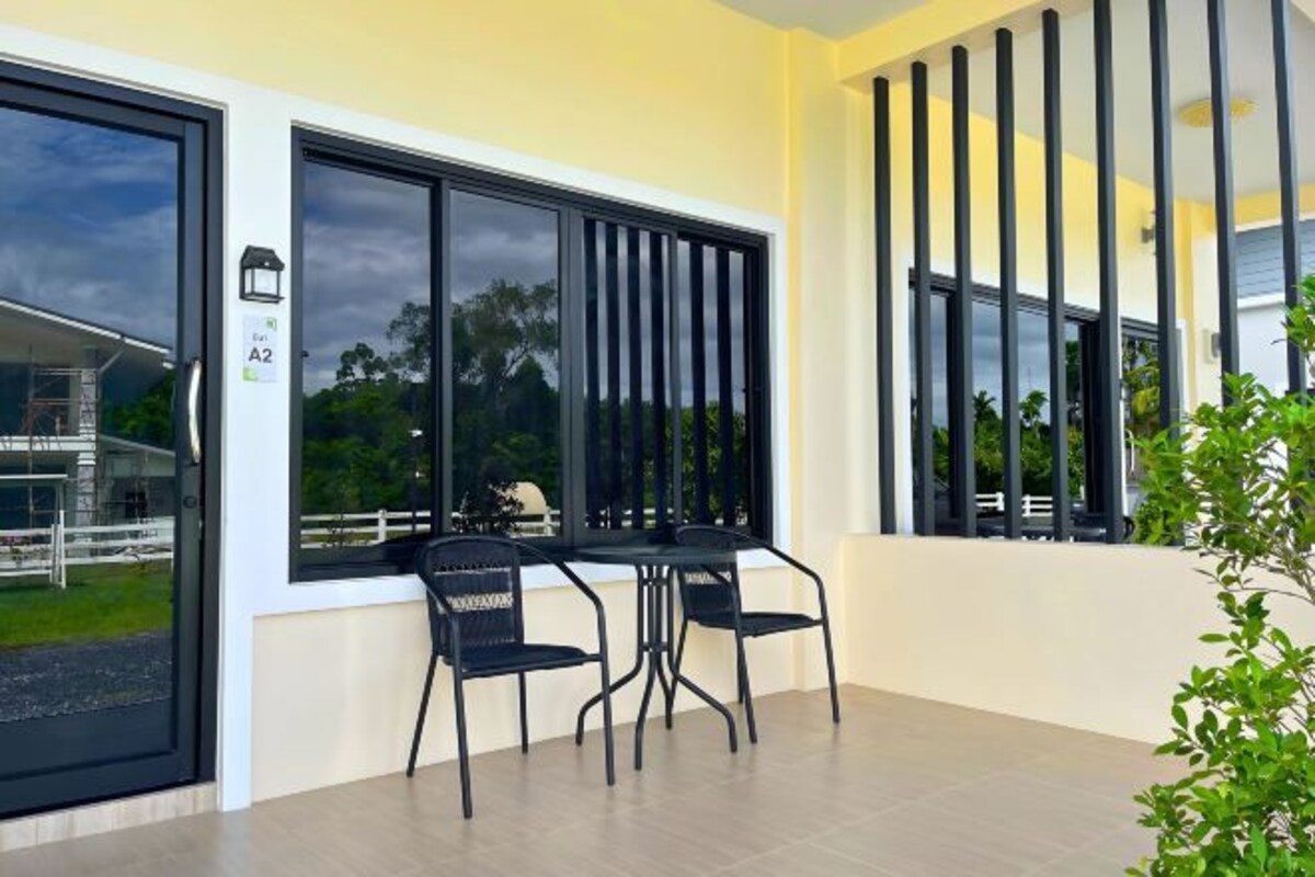 A modern room with large windows, a dining table with chairs, and a view of a fenced area outside.
