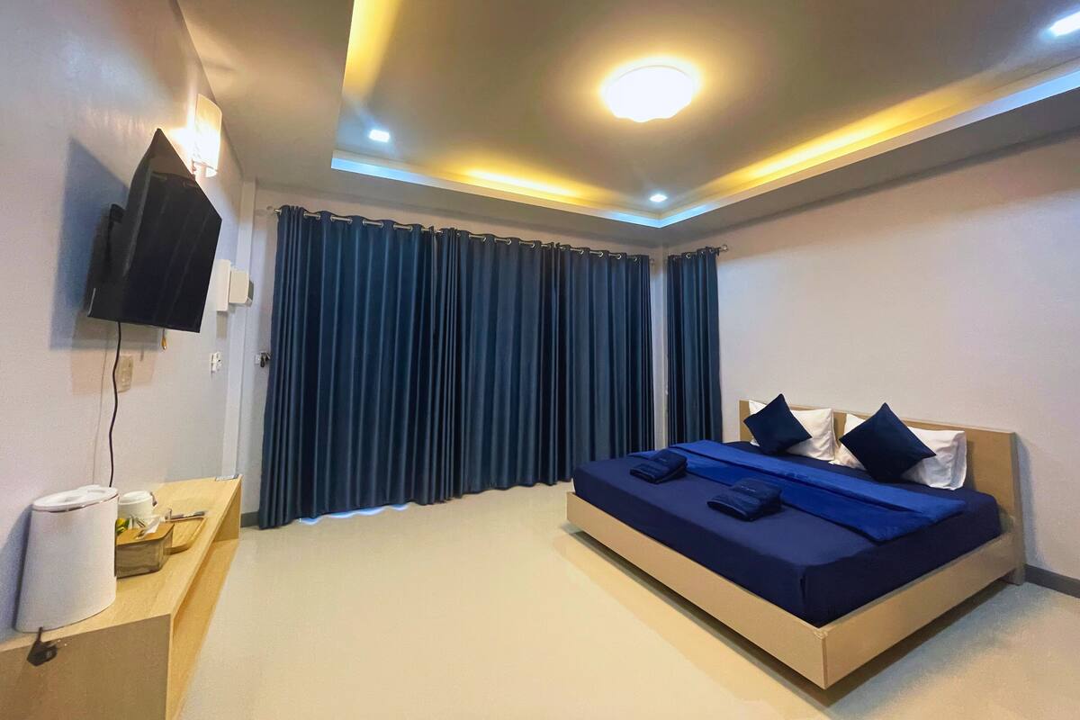 Une chambre d’hôtel moderne équipée d’un lit, d’un téléviseur à écran plat, d’une table de chevet avec une lampe et d’une grande fenêtre avec des rideaux.