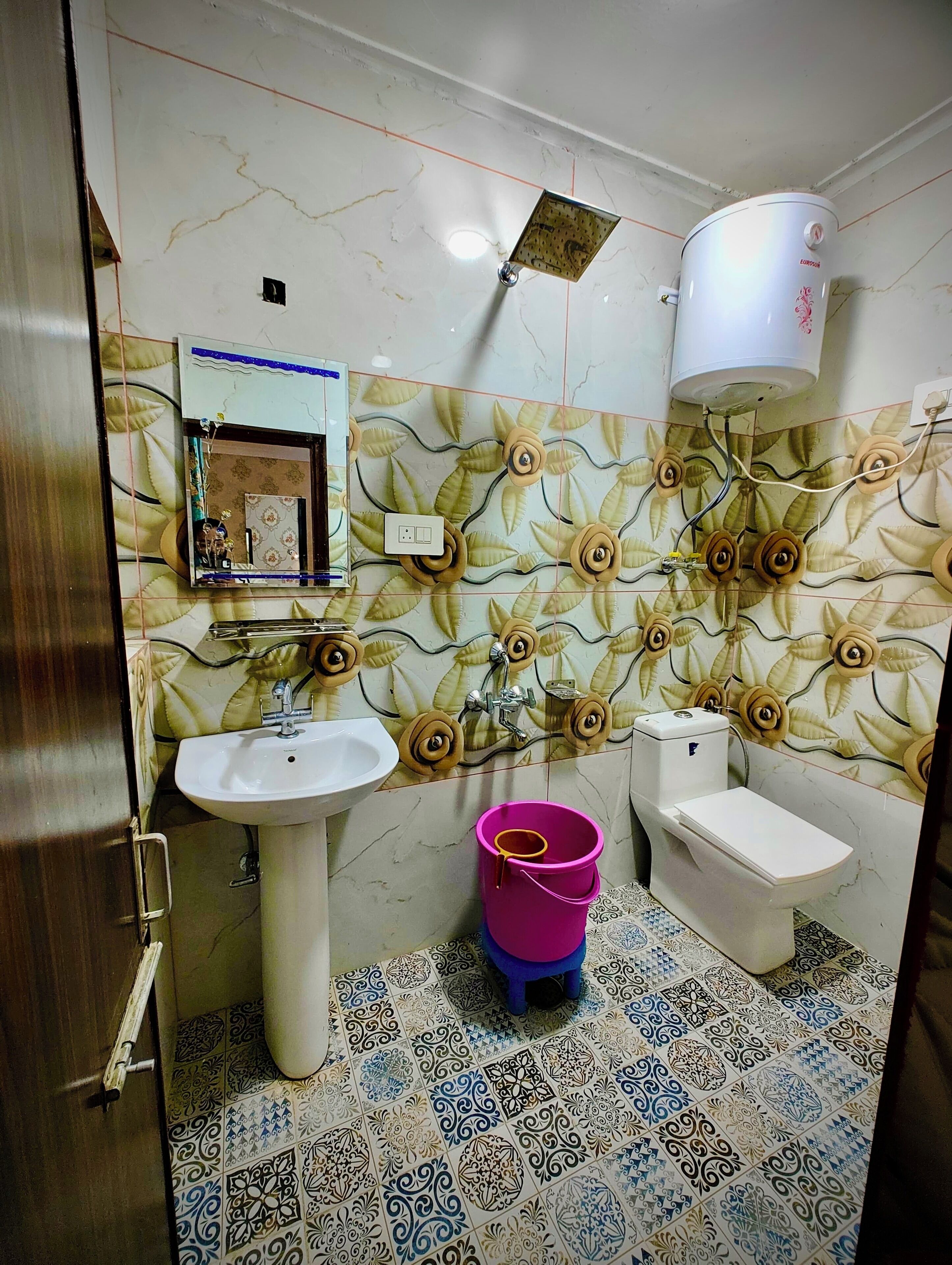 A bathroom with a white sink, toilet, and a water heater. The walls have a floral tile pattern, and the floor has a patterned tile design.