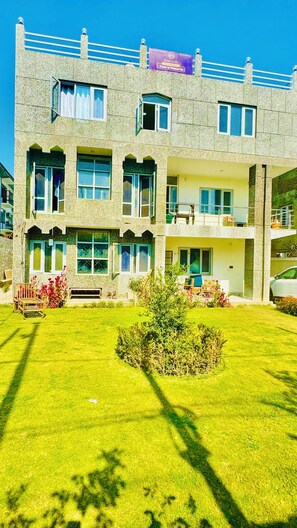 A multi-story hotel with a stone facade, balconies, and a well-maintained lawn. - Hotel Chitra operated by Zaara Resorts (Srinagar)