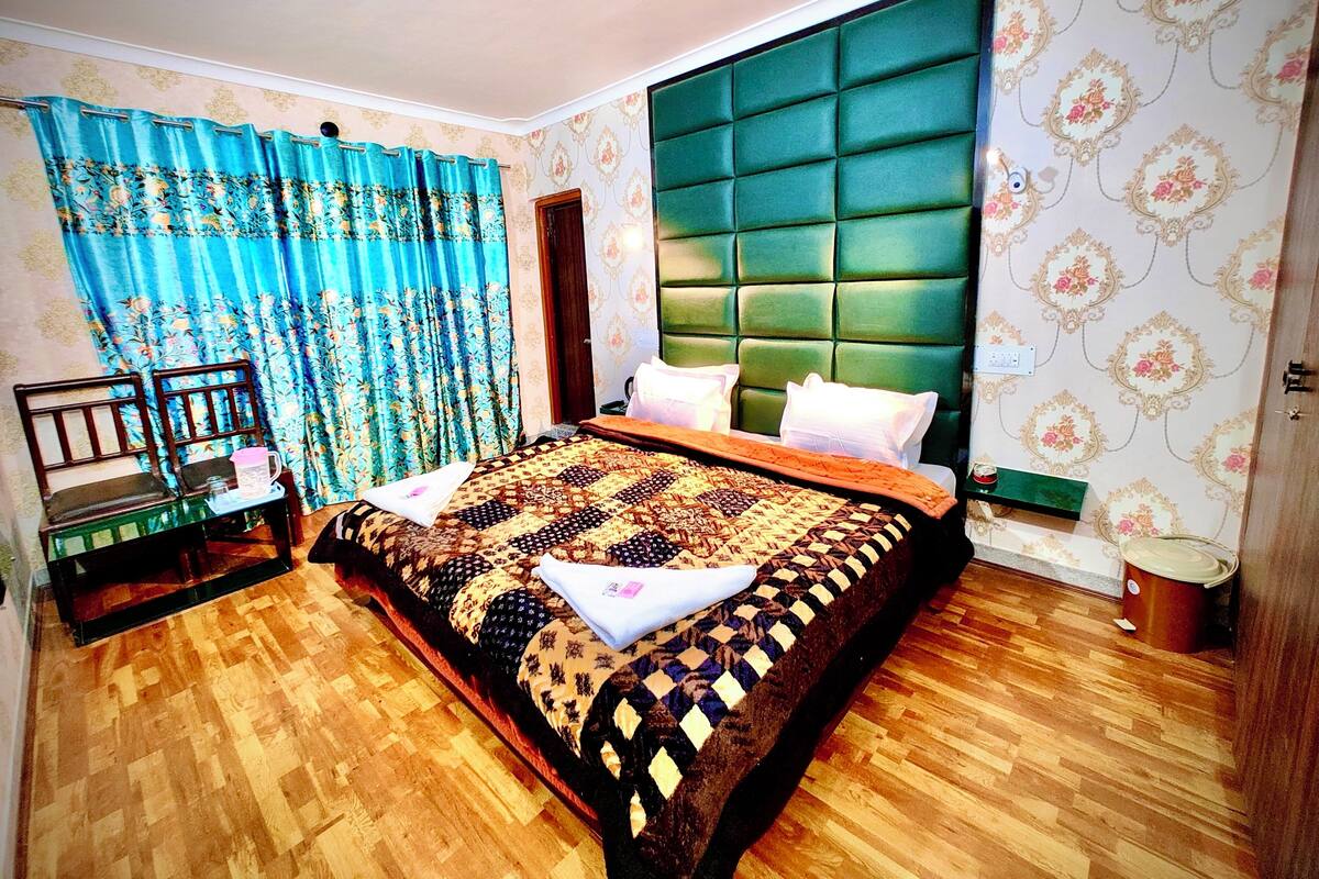 A bedroom with a large bed, a wooden chair, a nightstand, and a green upholstered headboard.