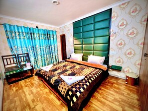 A bedroom with a large bed, a wooden chair, a nightstand, and a green upholstered headboard. - Hotel Chitra operated by Zaara Resorts (Srinagar)