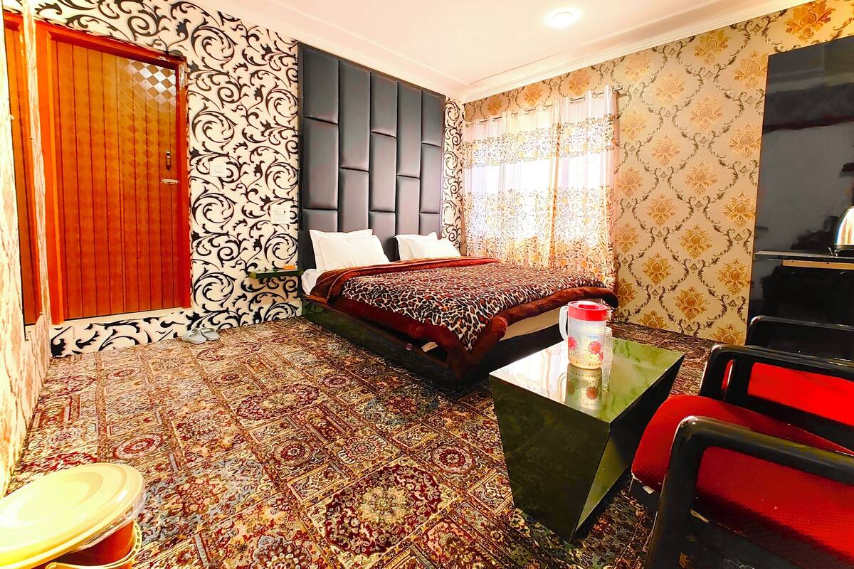 A bedroom with a bed, a coffee table, a red chair, a patterned carpet, and a wardrobe with a mirror.