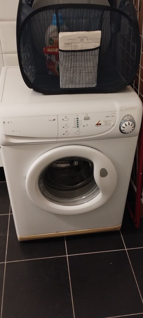 Een voorlader wasmachine met een bedieningspaneel, een voorraam en een mand voor wasgoed erboven.