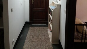 Ein schmaler Flur mit einer Holztür am Ende, einem kleinen Bücherregal und einem Teppichboden.