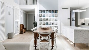 A modern kitchen with a marble countertop, a dining area with a wooden table and white chairs, and a bookshelf filled with books and decorative items.