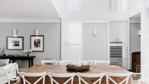 Een eethoek met een houten tafel omringd door witte stoelen, afbeeldingen aan de muur en een nest met eieren op de tafel.