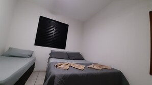 Um quarto pequeno e compacto com uma cama de solteiro, uma cama menor e uma janela com persianas.