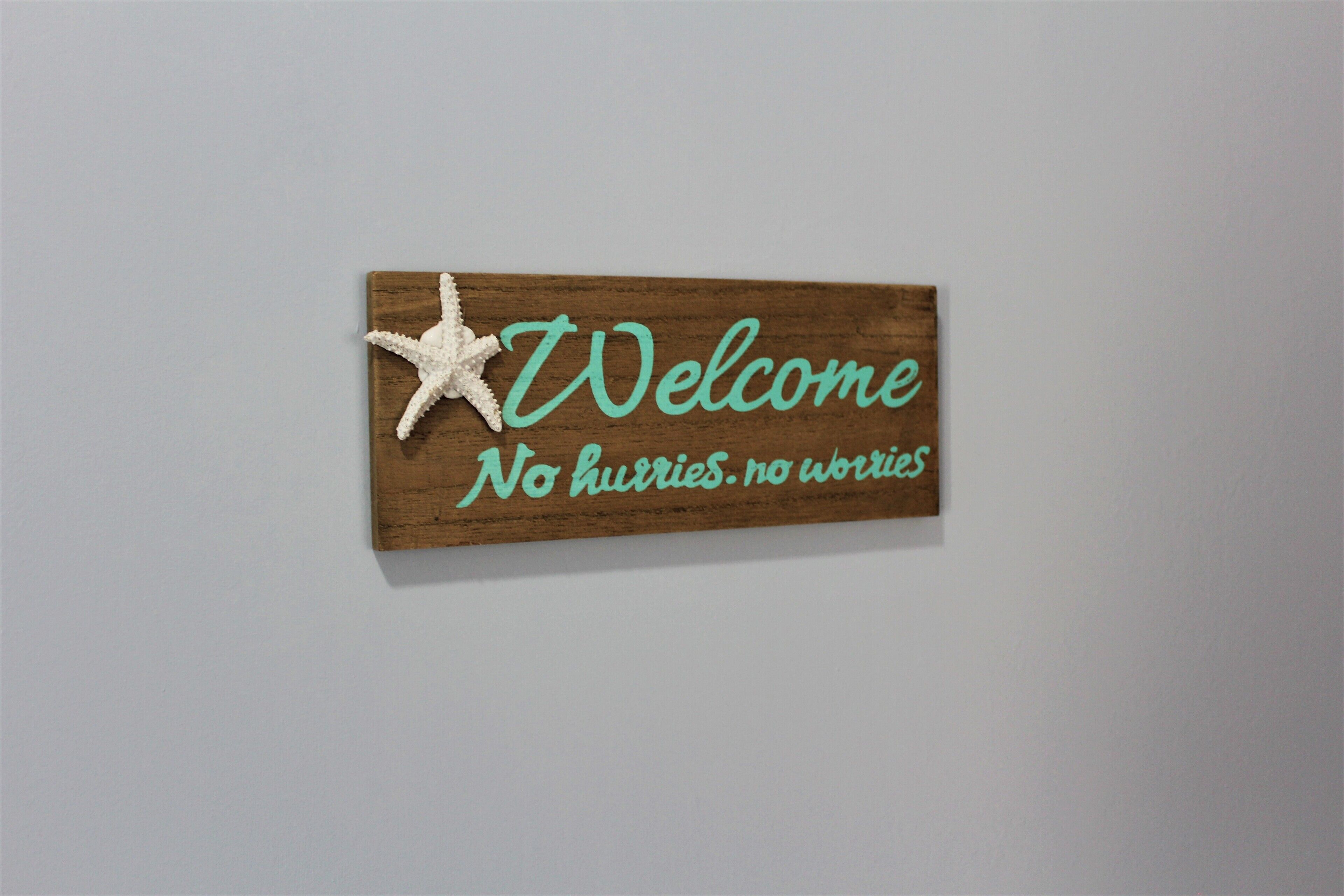 Uma placa de madeira com uma estrela-do-mar e o texto 'Welcome No hurries. No worries'.