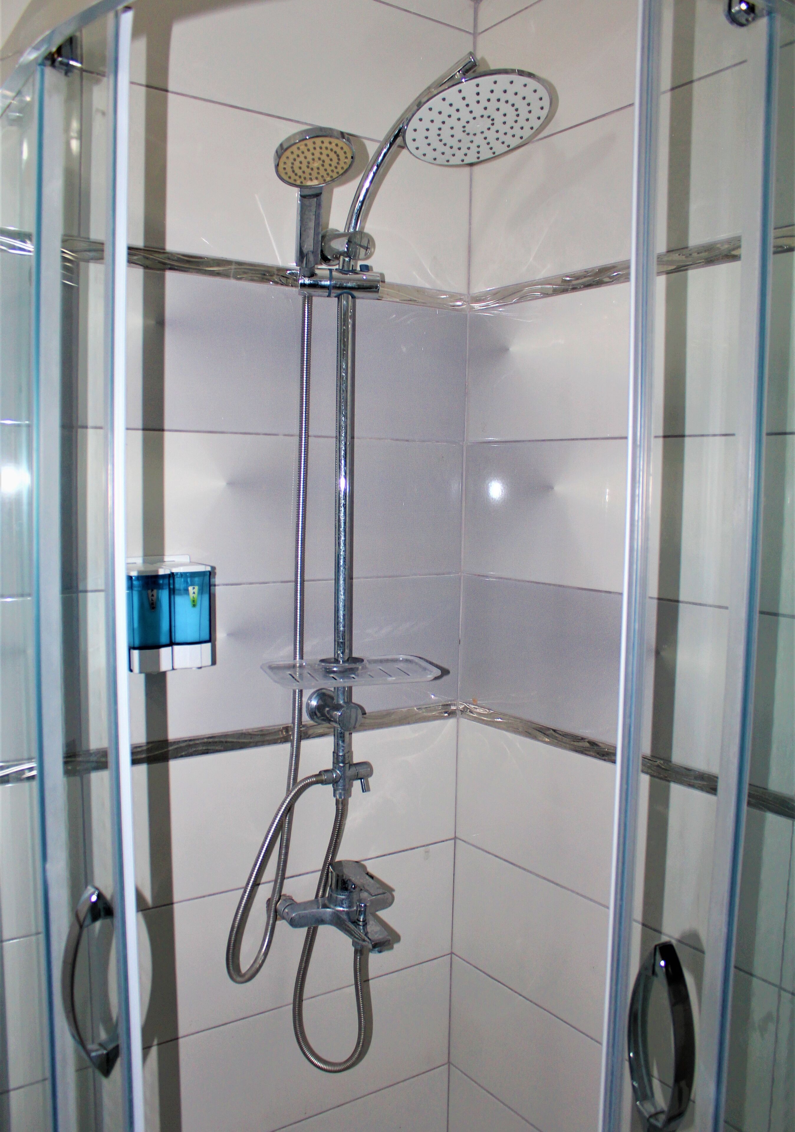 A shower enclosure with a handheld showerhead, a fixed showerhead, and a handheld shower hose.
