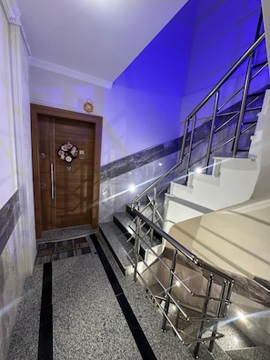 A modern hotel entrance with a wooden door, a marble staircase, and a blue-lit wall. - Mavi Restaurant & Apartments 1 (Didim)
