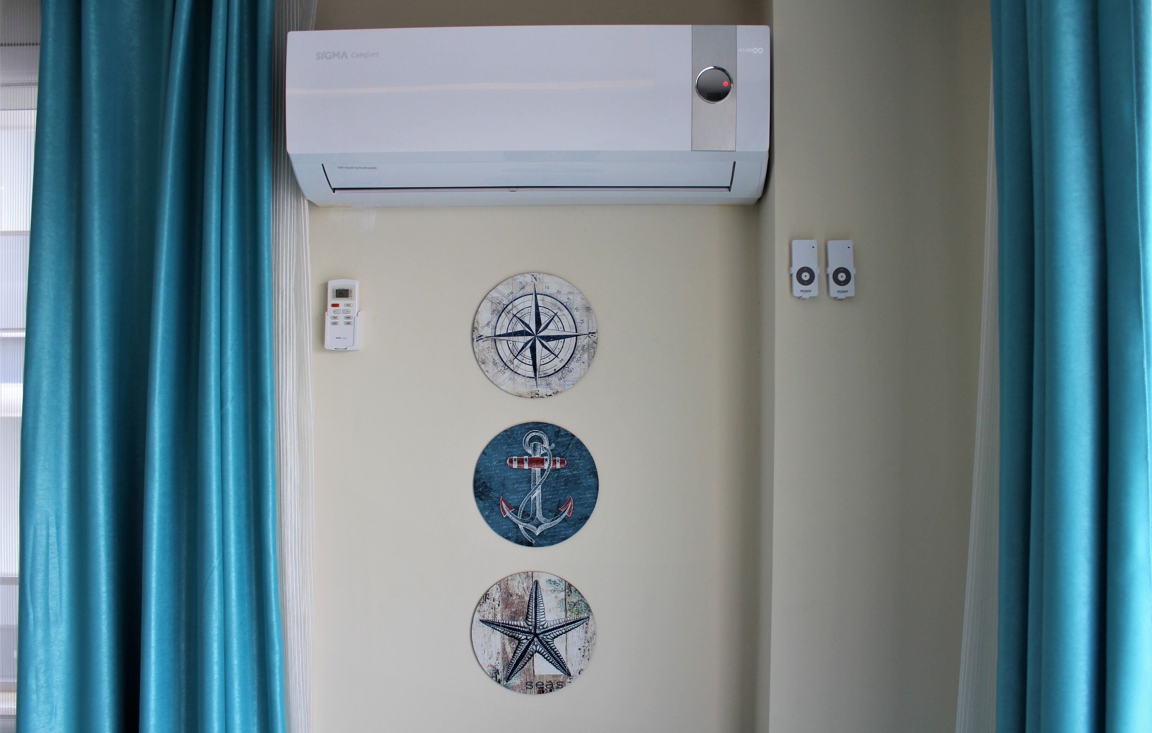 A wall-mounted air conditioner with a remote control, two wall-mounted thermostats, and three nautical-themed wall stickers.