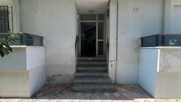 A building entrance with a tiled pavement, a staircase leading to an interior door, and a sign indicating availability for rent.