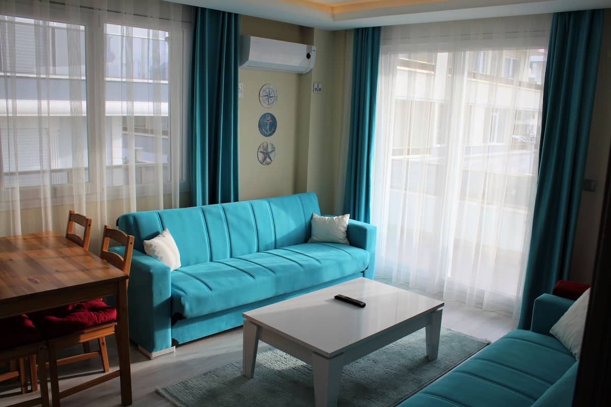 Uma sala de estar com um sofá verde-água, uma mesa de jantar de madeira e uma mesa de centro branca.