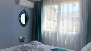 Una camera d'albergo con un letto, uno specchio, una finestra con tende leggere e un condizionatore d'aria.