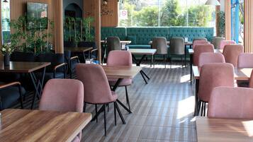 Un restaurante con mesas y sillas de madera, un sofá verde y ventanas amplias.