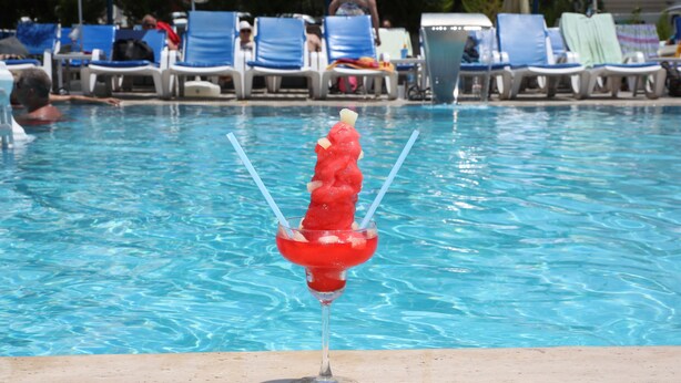 Area piscina con sedie a sdraio e un drink in un bicchiere.
