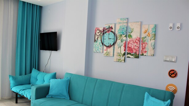 A teal sofa with matching cushions, a flat-screen TV mounted on the wall, and a floral artwork above it. - Mavi Restaurant & Apartments 1 (Didim)
