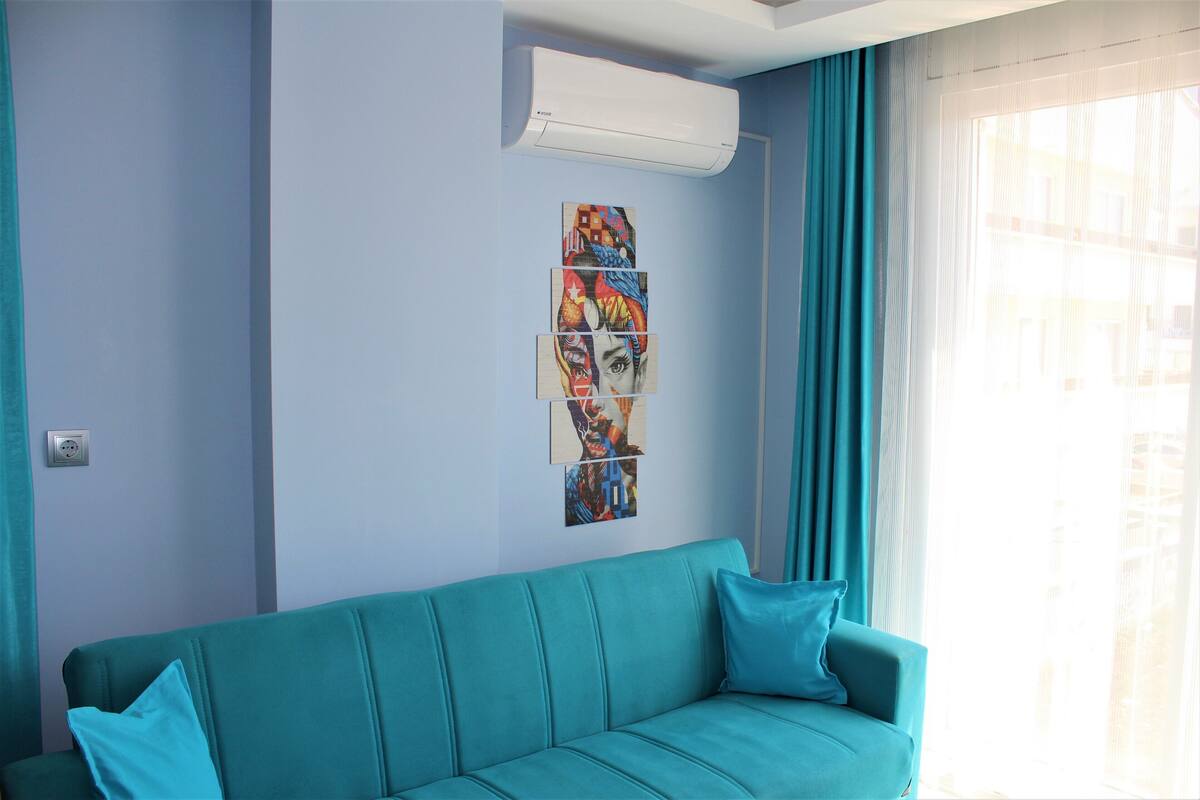 Um sofá azul-esverdeado com um ar condicionado moderno em cima e uma janela com cortinas.