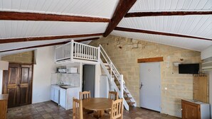 Un intérieur rustique avec une table à manger en bois, un coin cuisine et un escalier menant à une mezzanine.