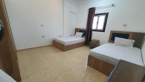Ett hotellrum med två sängar, ett litet fönster med gardiner och ett klinkergolv.