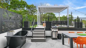 A modern outdoor patio with a grill, a black bathtub, and orange chairs. - Chic 3BR | Rooftop Views | Close to Beltline (Atlanta)