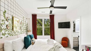 A bedroom with a bed, a ceiling fan, a window with curtains, a TV, and a door leading to a bathroom. - Chic 3BR | Rooftop Views | Close to Beltline (Atlanta)