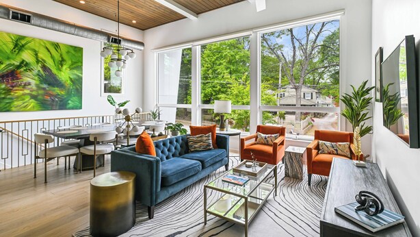 A spacious living area with a large window, a blue sofa, orange chairs, and a dining table. - Chic 3BR | Rooftop Views | Close to Beltline (Atlanta)