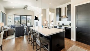 A modern kitchen with a large island, dark cabinetry, and a view of mountains.