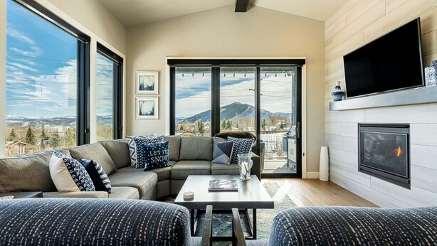 A modern living room with a sectional sofa, a flat-screen TV, a fireplace, and large windows offering a mountain view.