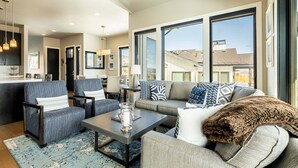 A modern living room with a sofa, armchairs, a coffee table, and large windows offering a view of the outside.