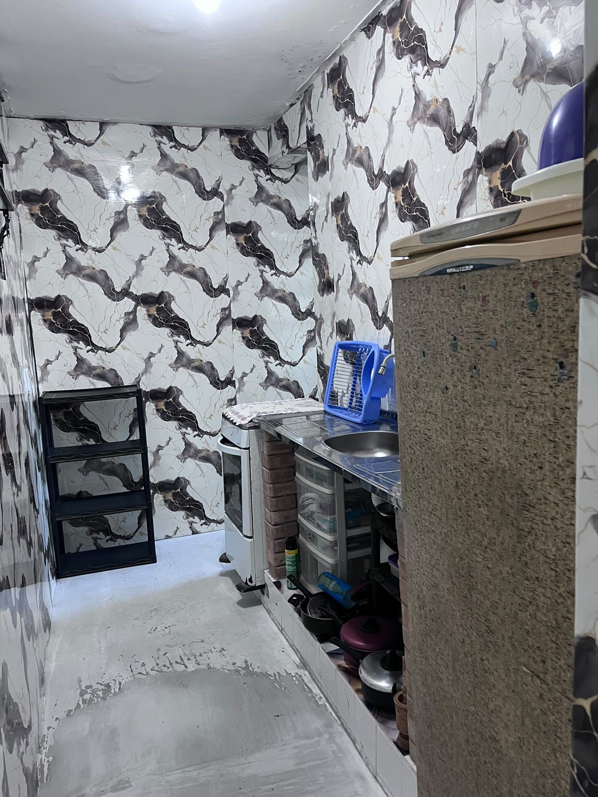 Uma cozinha compacta com painel de fundo de mármore, pia embutida e pequena geladeira.