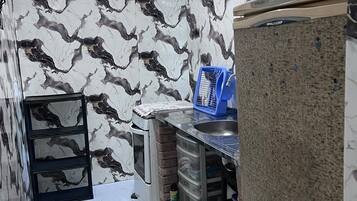 Uma cozinha compacta com painel de fundo de mármore, pia embutida e pequena geladeira.