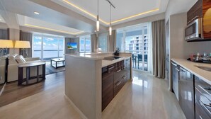 A modern hotel room with a central island, a dining area, a kitchen, and large windows offering a view of the city. - Beachfront Condo Fort Lauderdale Beach (Fort Lauderdale)