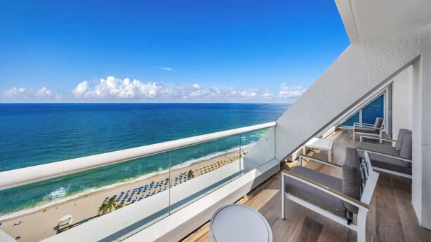 A balcony with a view of the ocean and beach, featuring a seating area with chairs and a table. - Beachfront Condo Fort Lauderdale Beach (Fort Lauderdale)