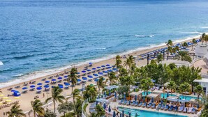 A beach resort with a pool area, beach chairs, umbrellas, and palm trees. - Beachfront Condo Fort Lauderdale Beach (Fort Lauderdale)