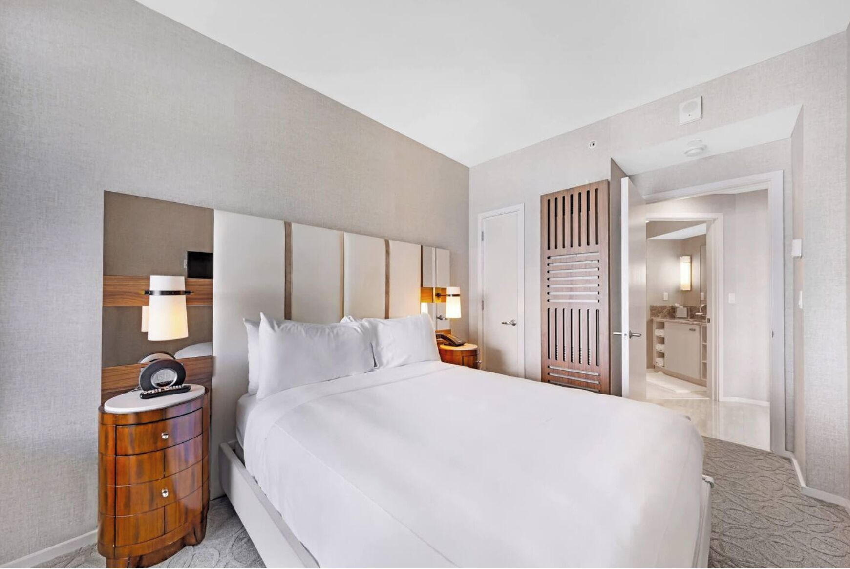 Une chambre d’hôtel avec un grand lit, des tables de chevet, une armoire et une salle de bain visible à travers une porte ouverte.
