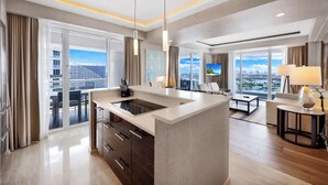 A modern hotel room with a central island kitchen, large windows with city views, a flat-screen TV, and a seating area with a view. - Beachfront Condo Fort Lauderdale Beach (Fort Lauderdale)