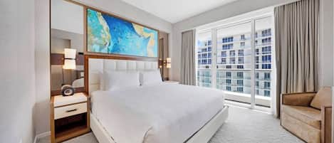 Hotelkamer met een groot bed, een bureau met lamp, een stoel en een groot raam met uitzicht op de stad.