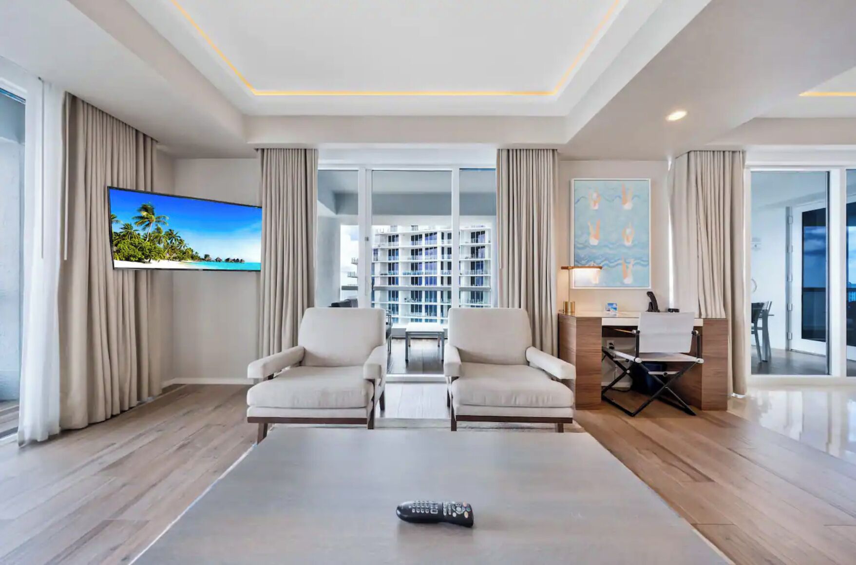 A modern hotel room with a large flat-screen TV, a sofa, a coffee table, and a desk with a chair.