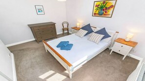 Ein Schlafzimmer mit einem Bett, zwei Nachttischen, einer Kommode, einem Sessel und einer Wand mit einem gerahmten Bild.