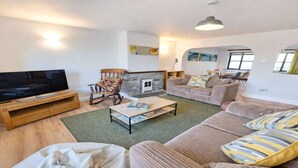 A living room with a television, a fireplace, a sofa, and a rocking chair. - Rockham Bay View - Sleeps 6 Mortehoe (Woolacombe)