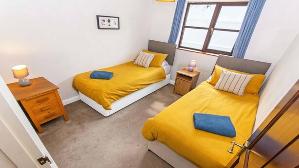 A bedroom with two single beds, a nightstand, a bedside table, and a window with curtains. - Rockham Bay View - Sleeps 6 Mortehoe (Woolacombe)