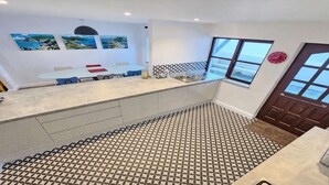A modern kitchen with a patterned floor, a dining area with blue chairs, and artwork on the walls. - Rockham Bay View - Sleeps 6 Mortehoe (Woolacombe)